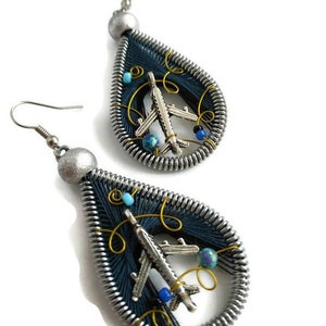 May include: A pair of silver teardrop-shaped earrings with blue wire wrapped around the teardrop. Each teardrop has a silver airplane charm inside with blue and turquoise beads.