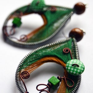 Könnte beinhalten: Ein Paar grüne und braune drahtgewickelte Ohrringe mit einem grün-weiß gepunkteten Knopf und einer grünen Perle. Die Ohrringe sind aus Kupferdraht gefertigt und haben eine silberne Oberfläche.