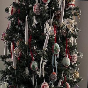 May include: A decorated Christmas tree with various ornaments and white candle-shaped lights. The ornaments are round, with red, white, and blue ribbons. Some ornaments have floral patterns, and others have glitter.