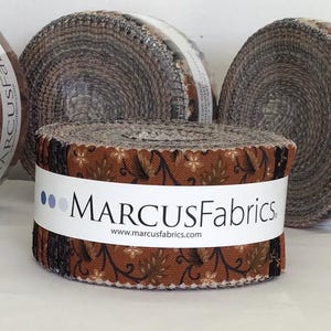 May include: Four rolls of fabric strips from Marcus Fabrics, each secured with a white paper band. The rolls feature various patterns in shades of brown, black, and tan. One band clearly displays the text Marcus Fabrics and Midnight Cheddar.
