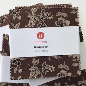 May include: A stack of fabric squares with a floral pattern in brown, black, and beige. The fabric is labeled "Andover Bridgeport Jo Morton" with a red logo. The edges of the fabric are jagged.