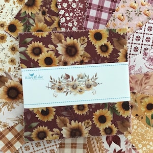 May include: A stack of square fabric swatches featuring various autumn-themed patterns including sunflowers, pumpkins, plaid, and floral designs. A white paper band wraps around the center with the text Riley Blake Designs Harvest on the Prairie.