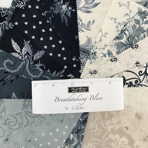 Peut inclure: Une collection de carr&eacute;s de tissu dispos&eacute;s en &eacute;ventail, pr&eacute;sentant diverses nuances de bleu marine, bleu ardoise et cr&egrave;me avec des motifs floraux et botaniques. Une &eacute;tiquette blanche indique "moda FABRICS+SUPPLIES Breathtaking Blues by 3 Sisters" avec une r&egrave;gle.