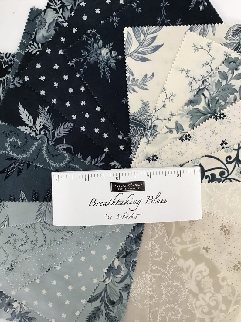 Peut inclure: Une collection de carr&eacute;s de tissu dispos&eacute;s en &eacute;ventail, pr&eacute;sentant diverses nuances de bleu marine, bleu ardoise et cr&egrave;me avec des motifs floraux et botaniques. Une &eacute;tiquette blanche indique "moda FABRICS+SUPPLIES Breathtaking Blues by 3 Sisters" avec une r&egrave;gle.
