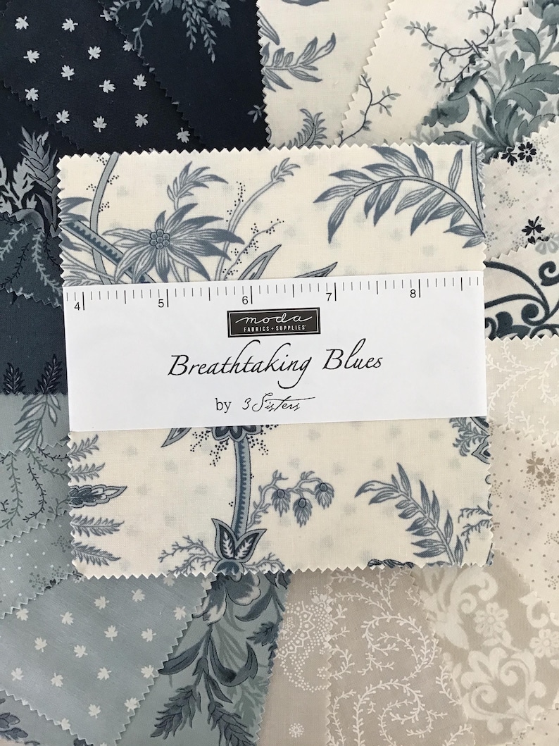 Peut inclure: Une pile de carr&eacute;s de tissu pr&eacute;sentant divers motifs floraux et botaniques bleus et cr&egrave;me. Une bande de papier blanc entoure le centre, imprim&eacute;e avec "moda FABRICS+SUPPLIES", "Breathtaking Blues" et "by 3 Sisters", avec une r&egrave;gle de 12,7 cm.