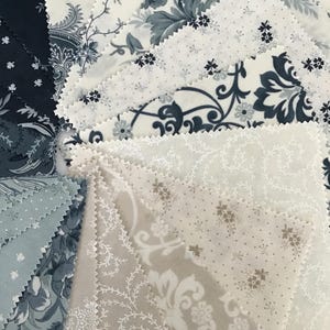 Peut inclure: Un ensemble d'&eacute;chantillons de tissu carr&eacute;s dispos&eacute;s en &eacute;ventail, pr&eacute;sentant divers motifs dans des tons bleu marine, gris ardoise, cr&egrave;me et beige. Les pi&egrave;ces de tissu ont des bords dentel&eacute;s et affichent des motifs floraux et damass&eacute;s.