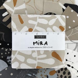 May include: A collection of fabric squares with various patterns and colors. The dominant square features a beige background with white and orange leaf-like designs. The text "MIRA" is visible, along with the designer's name. A ruler is placed on top of the fabric.