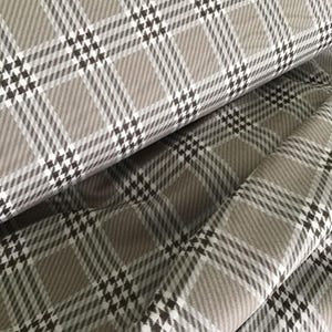 May include: Close-up of a folded fabric with a classic plaid pattern. The fabric features a repeating pattern of tan, white, and black squares and lines. The fabric is folded over itself, showing the texture and depth of the material.