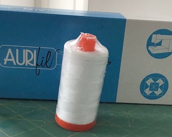 May include: A white spool of Aurifil thread with an orange plastic top and a blue and white box with the Aurifil logo. The box also has a sewing machine and a quilt block design.