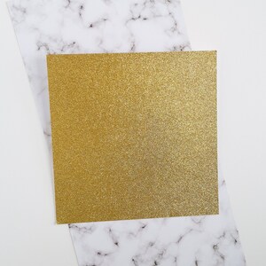May include: A gold glitter card on top of a white marble background.
