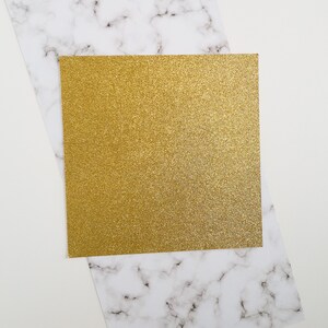 May include: A gold glitter card on a white marble background.