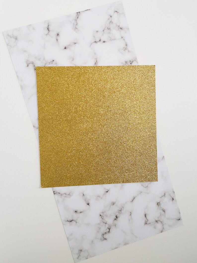 May include: A gold glitter card on a white marble background.