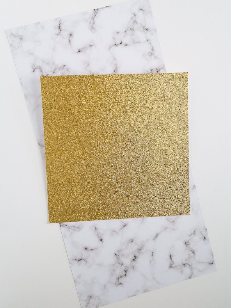 May include: A gold glitter card on top of a white marble background.