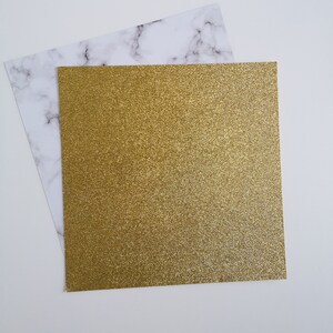 May include: A sheet of gold glitter paper on a white marble background.