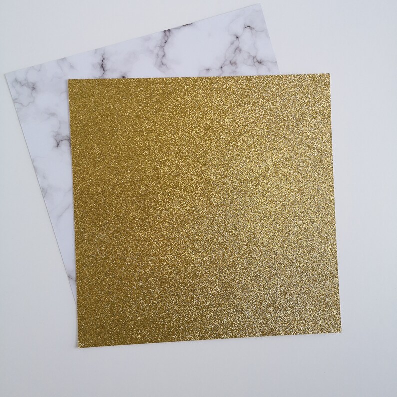 May include: A sheet of gold glitter paper on a white marble background.