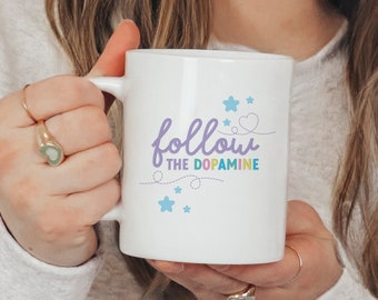 May include: White ceramic mug with a purple and blue design that says "follow the dopamine" with a heart and stars.