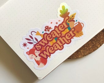 以下が含まれることがあります： キツネ、葉っぱ、そして「sweater weather」というテキストが書かれた秋色のステッカーです。