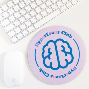 May include: A purple round mouse mat with a blue brain graphic and the text "Hyperfocus Club" in pink and blue lettering.