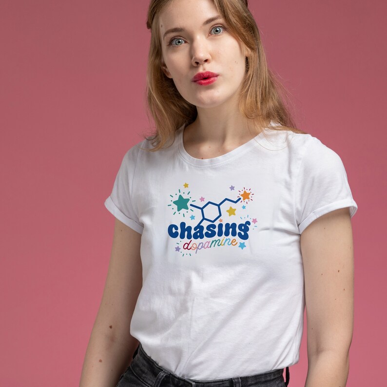 May include: White t-shirt featuring a colourful graphic of a dopamine molecule and the text "chasing dopamine" surrounded by stars.