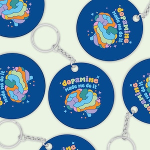 May include: A set of four blue round keychains with a colourful brain graphic and the text "dopamine made me do it".