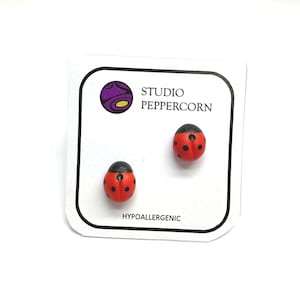 May include: A pair of red and black ladybug stud earrings on a white card with the text "Studio Peppercorn" and "Hypoallergenic".