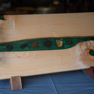 May include: A wooden serving tray with a green and brown epoxy river inlay and black metal handles. The tray is on wooden legs.