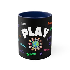 May include: Black coffee mug with a blue rim. The mug features the word "PLAY" in white letters and a circle of children holding hands around a globe. The word "PLAY" is surrounded by the word "play" in different languages, including Spanish, French, German, Italian, Polish, Portuguese, Japanese, Arabic, Hebrew, and Hindi.