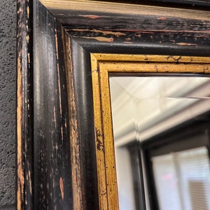 May include: A black and gold framed mirror with a distressed finish. The frame has a wide, ornate design with a gold accent.