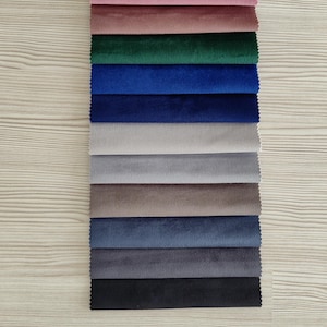 May include: A vertical stack of rectangular fabric swatches featuring a velvet texture. The colors include brown, pink, mauve, emerald green, royal blue, navy, light gray, medium gray, taupe, slate blue, charcoal, and black in a layered arrangement.