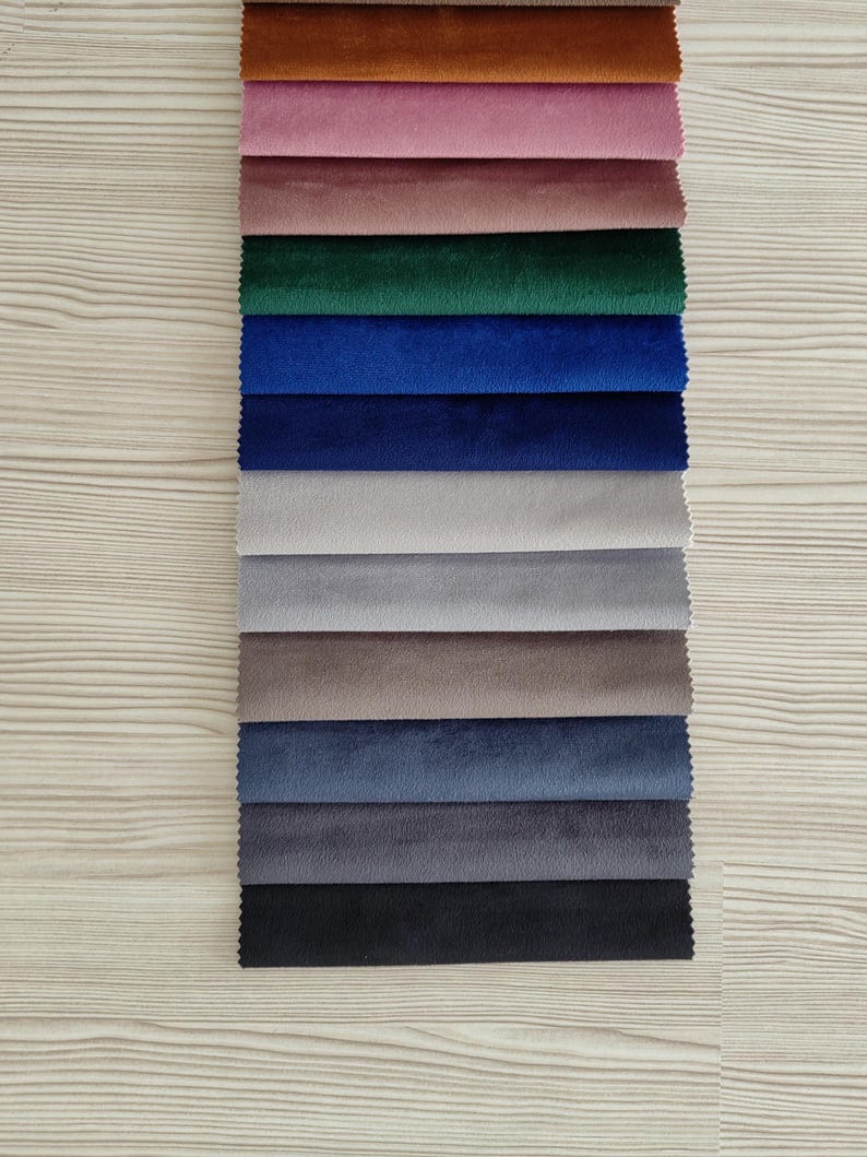 May include: A vertical stack of rectangular fabric swatches featuring a velvet texture. The colors include brown, pink, mauve, emerald green, royal blue, navy, light gray, medium gray, taupe, slate blue, charcoal, and black in a layered arrangement.