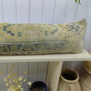 May include: A long, rectangular pillow with a light blue and yellow patterned fabric. The pillow is sitting on a white shelf with a wooden frame.