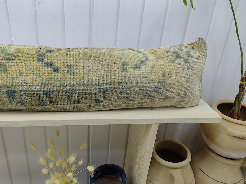 May include: A long, rectangular pillow with a light blue and yellow patterned fabric. The pillow is sitting on a white shelf with a wooden frame.