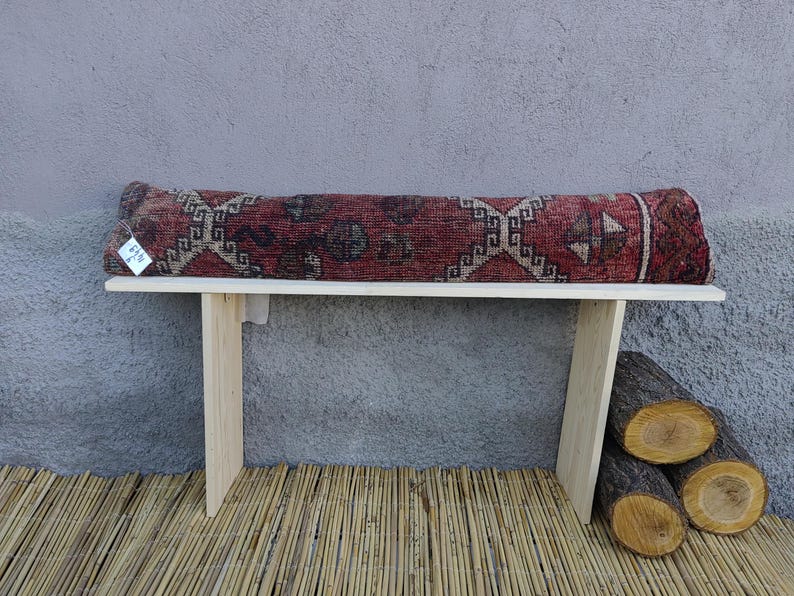 May include: A wooden bench with a red, black, and white patterned cushion. The bench is sitting on a woven bamboo mat.