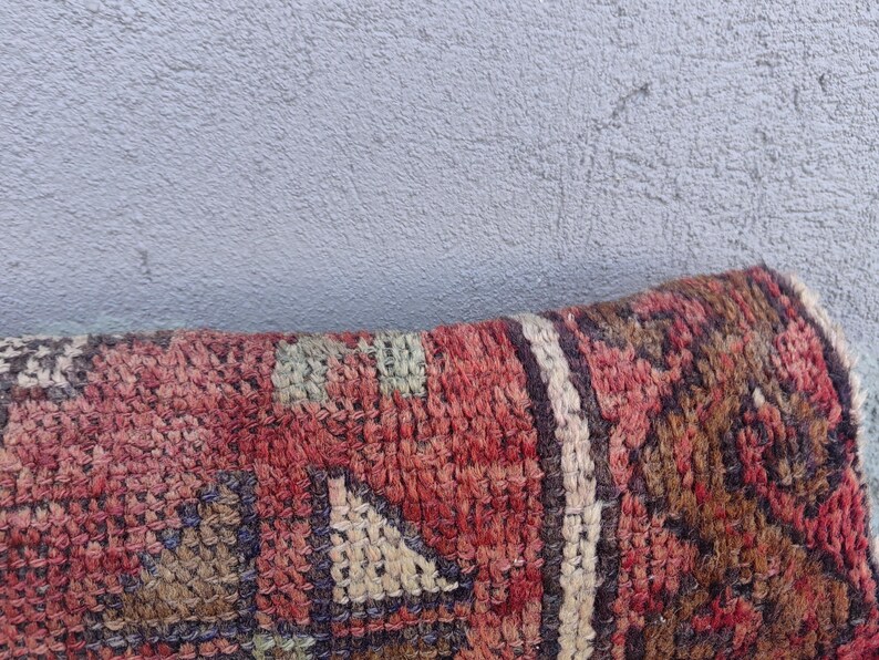 May include: Close-up of a red, brown, and cream patterned rug with a geometric design. The rug is made of woven fabric and has a soft, textured surface.