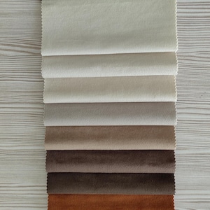May include: A vertical stack of seven rectangular fabric swatches arranged in a gradient from light cream to dark brown. Each swatch features a soft, matte texture with clean, pinked edges, showcasing a neutral color palette of beige, tan, and brown.