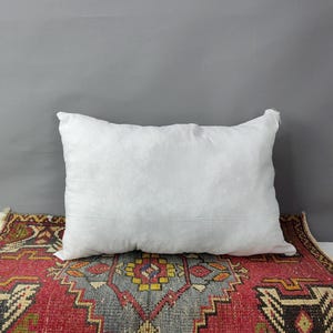 May include: A white pillow with a plain white cover sits on top of a red, blue, and yellow patterned rug.