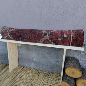 May include: A wooden bench with a red, white, and blue patterned rug cushion. The bench is sitting on a bamboo mat.