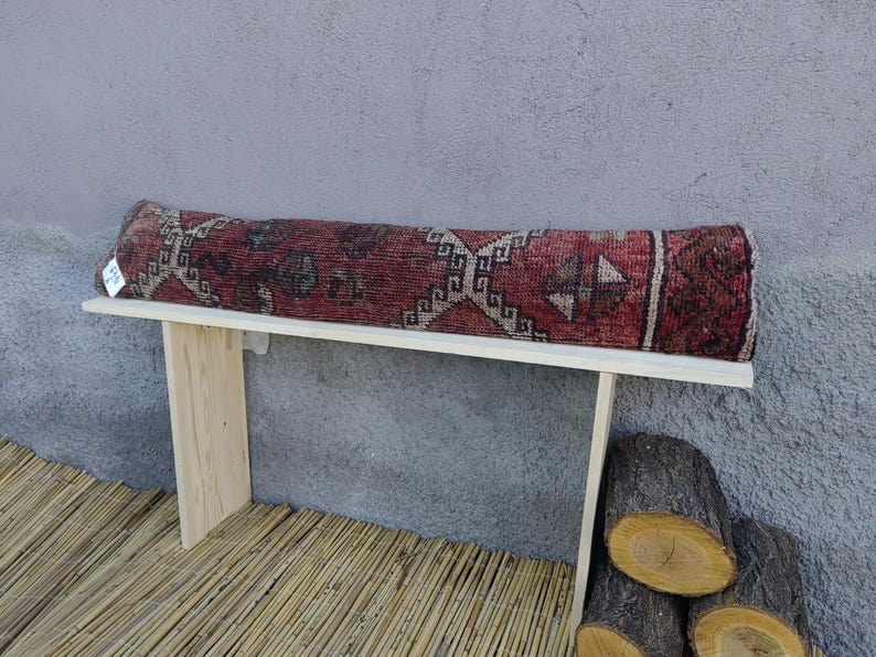 May include: A wooden bench with a red, white, and blue patterned rug cushion. The bench is sitting on a bamboo mat.