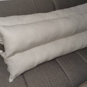 May include: Two white rectangular pillows on a gray couch. The pillows are long and narrow, and they are stacked on top of each other.