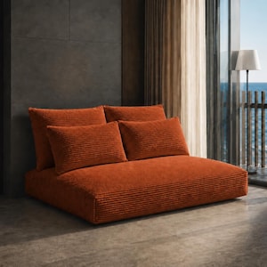 Könnte beinhalten: Ein niedriges Sofa aus rostfarbenem Kordstoff mit einer breiten, rechteckigen Basis, zwei großen Rückenkissen und zwei kleineren, passenden rechteckigen Zierkissen, die alle mit einem strukturierten, horizontal gerippten Stoff bezogen sind.