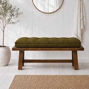May include: A rectangular, tufted bench cushion in a deep olive green color. The cushion features a textured, fabric surface with multiple stitched indentations across its length, designed to fit securely on top of a wooden bench seat.