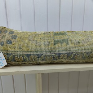 May include: A long, rectangular pillow with a blue and yellow patterned fabric. The pillow is sitting on a white shelf with the number "614" written on a tag attached to the pillow.