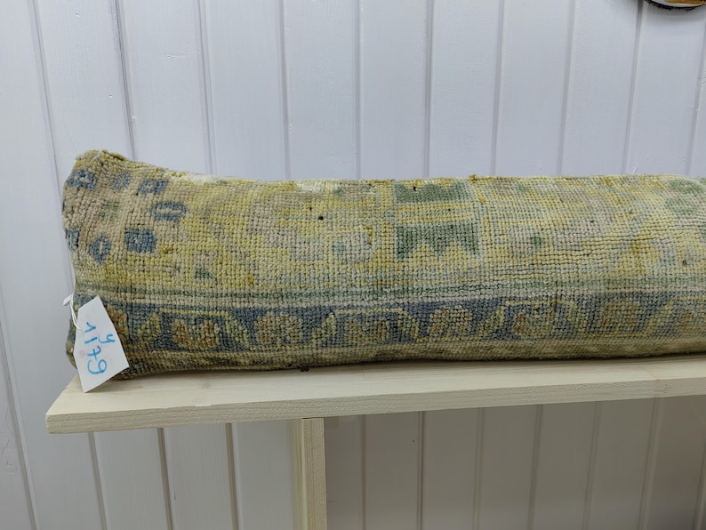 May include: A long, rectangular pillow with a blue and yellow patterned fabric. The pillow is sitting on a white shelf with the number "614" written on a tag attached to the pillow.
