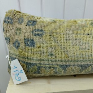 May include: A long, rectangular pillow with a blue and yellow patterned design. The pillow is made of a soft, woven fabric and has a tag attached to it that says "6+11".