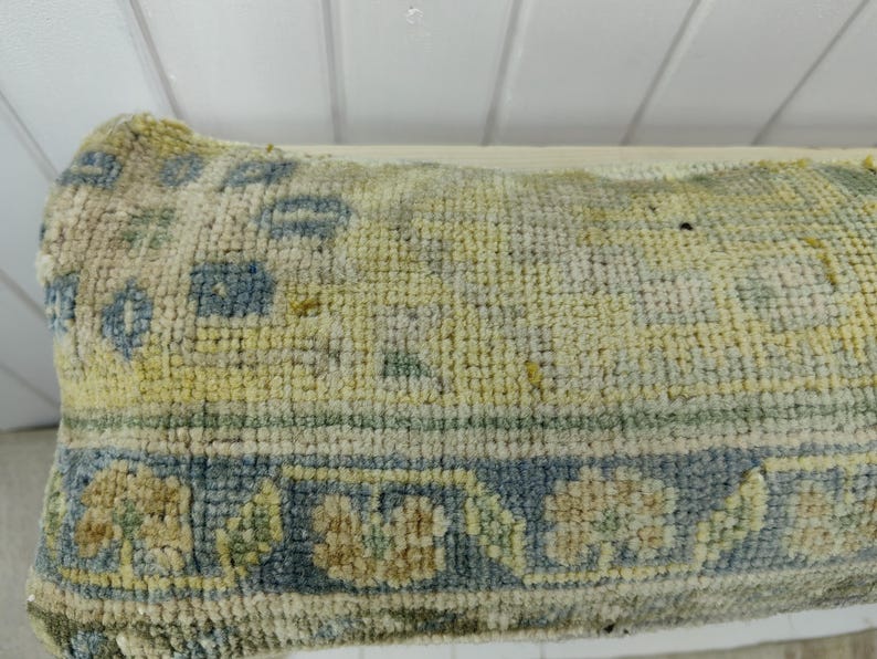 May include: A close-up of a light blue and cream colored rug with a geometric pattern. The rug has a worn and faded appearance.