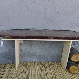 May include: A wooden bench with a patterned cushion. The bench has two legs on each side and is sitting on a woven bamboo mat.