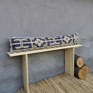 Puede incluir: Un banco de madera con un cojín estampado. El cojín es azul y blanco con un diseño geométrico. El banco está sentado en un suelo de madera con una estera de bambú.