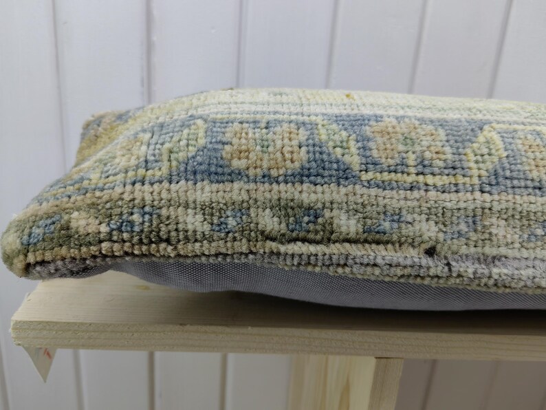 May include: A rectangular pillow with a blue, beige, and green patterned fabric. The pillow has a light gray backing and is sitting on a wooden surface.