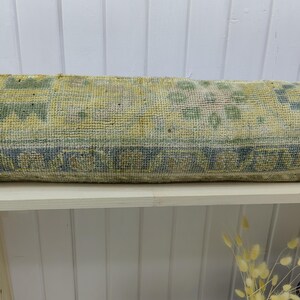 May include: A long, rectangular, light green and blue patterned throw pillow. The pillow is made of a soft, woven fabric and is sitting on a white shelf.