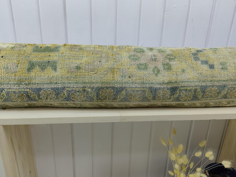 May include: A long, rectangular, light green and blue patterned throw pillow. The pillow is made of a soft, woven fabric and is sitting on a white shelf.